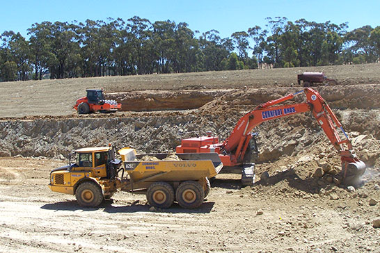 Earth works photo Excavator loading dump truck with roller in background